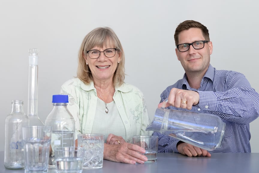 Agnetha och Johan h&auml;ller upp vatten i glas ur tillbringare