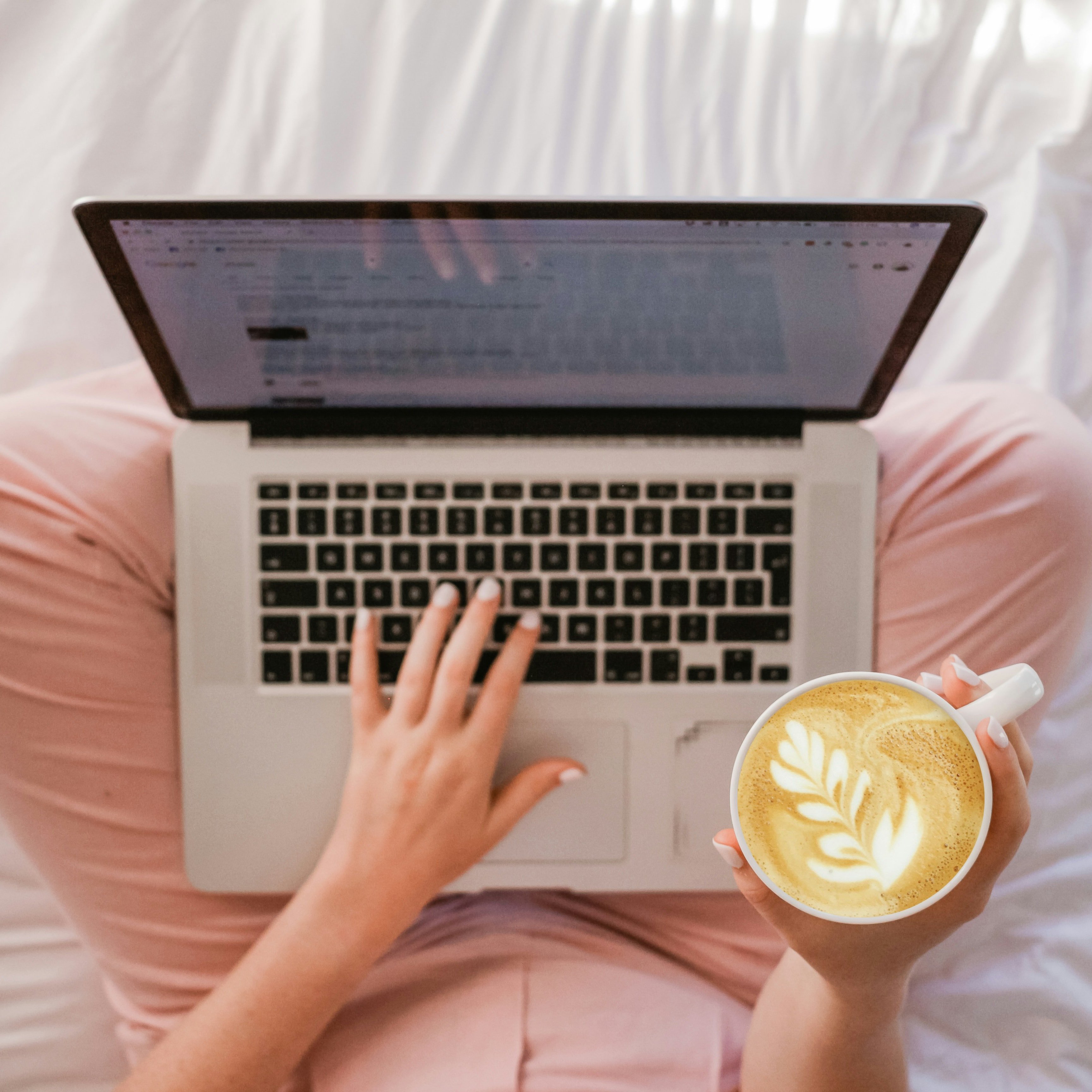 Laptop och kaffekopp i knäet på person med rosa byxor, sedd uppifrån