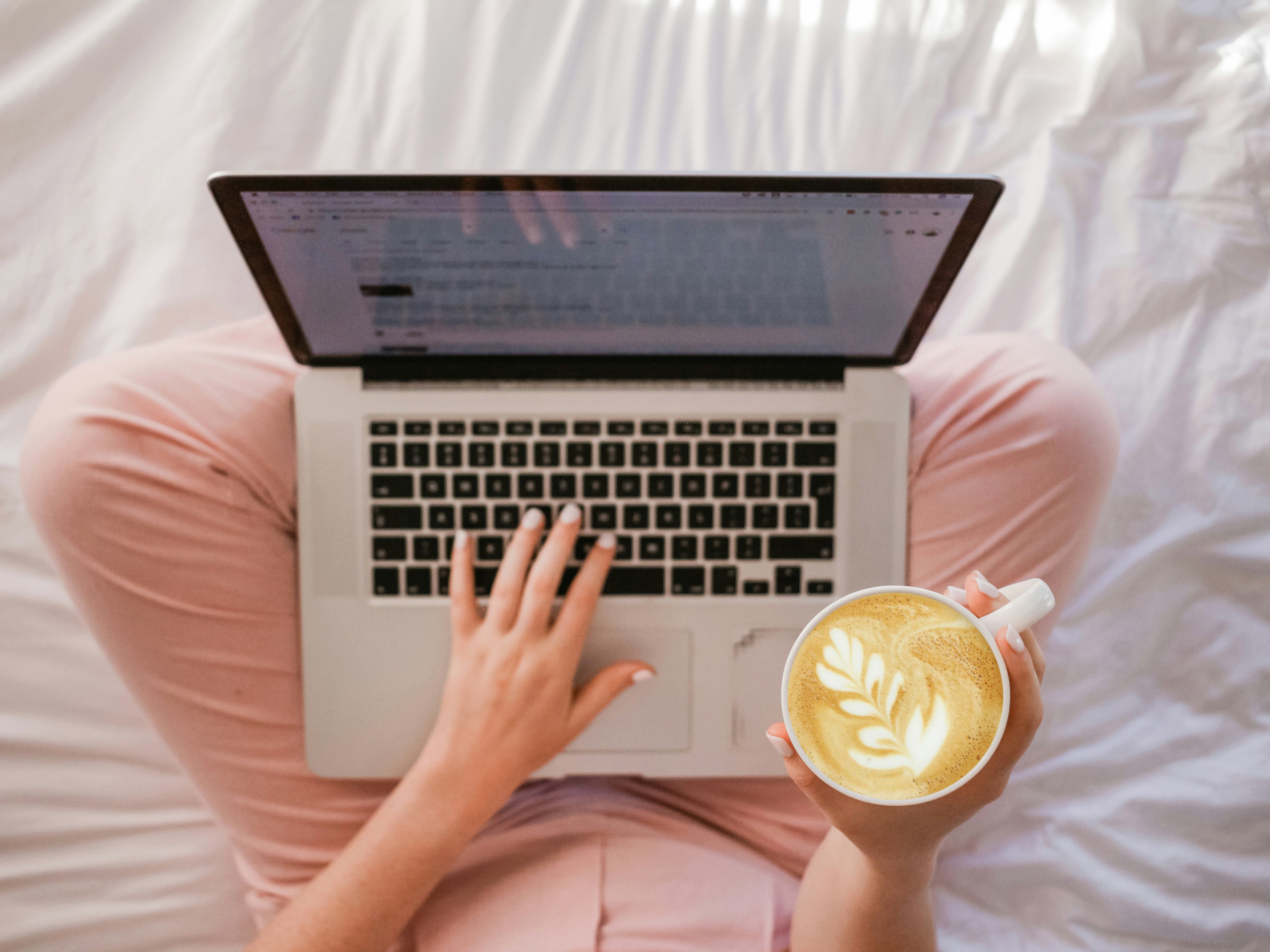 Laptop och kaffekopp i knäet på person med rosa byxor, sedd uppifrån